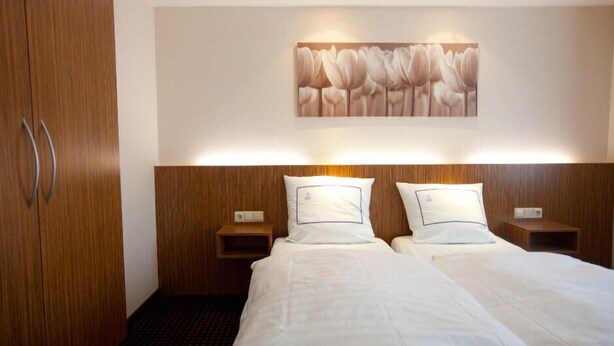 Ein Hotelzimmer mit einem hölzernen Kopfteil, zwei Nachttischen, einem großen Bett mit weißer Bettwäsche und einem Wandbild von Tulpen.