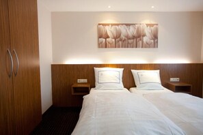 Une chambre d’hôtel avec une tête de lit en bois, deux tables de chevet, un grand lit avec du linge de lit blanc et une œuvre d’art représentant des tulipes, accrochée au mur.