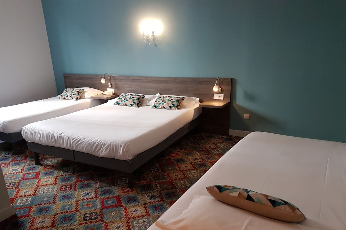 A hotel room with two single beds, a patterned carpet, and a wall-mounted light fixture.