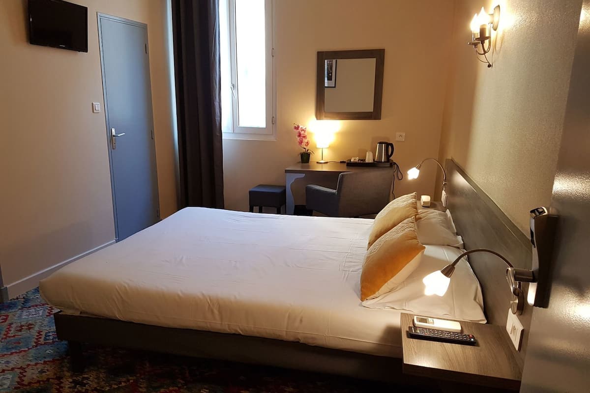 A hotel room with a bed, bedside table, lamp, and a TV on the wall.