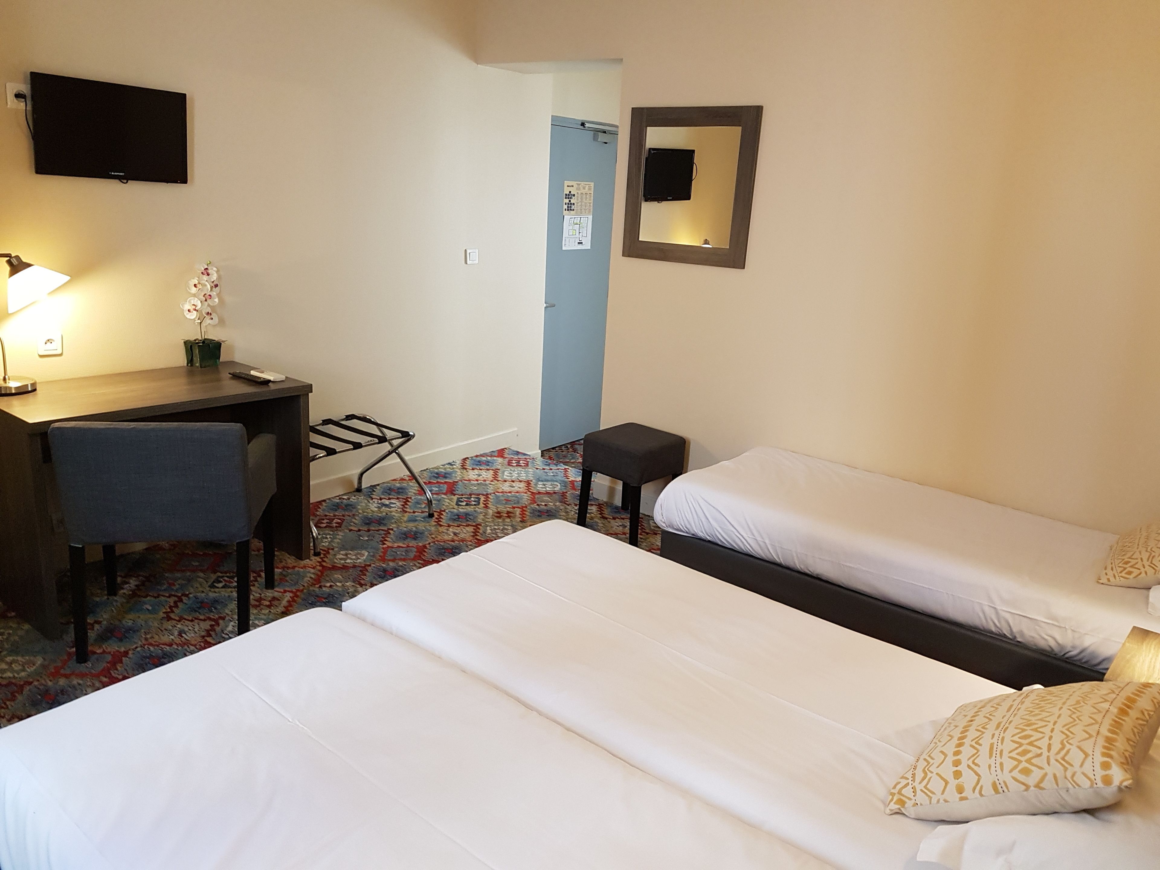 A hotel room with two beds, a desk, a chair, a TV, and a small table.