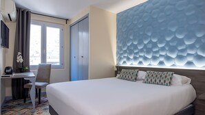 A hotel room with a bed, a desk, a chair, a window, and a decorative wall. - Hôtel Danieli Avignon (Avignon)