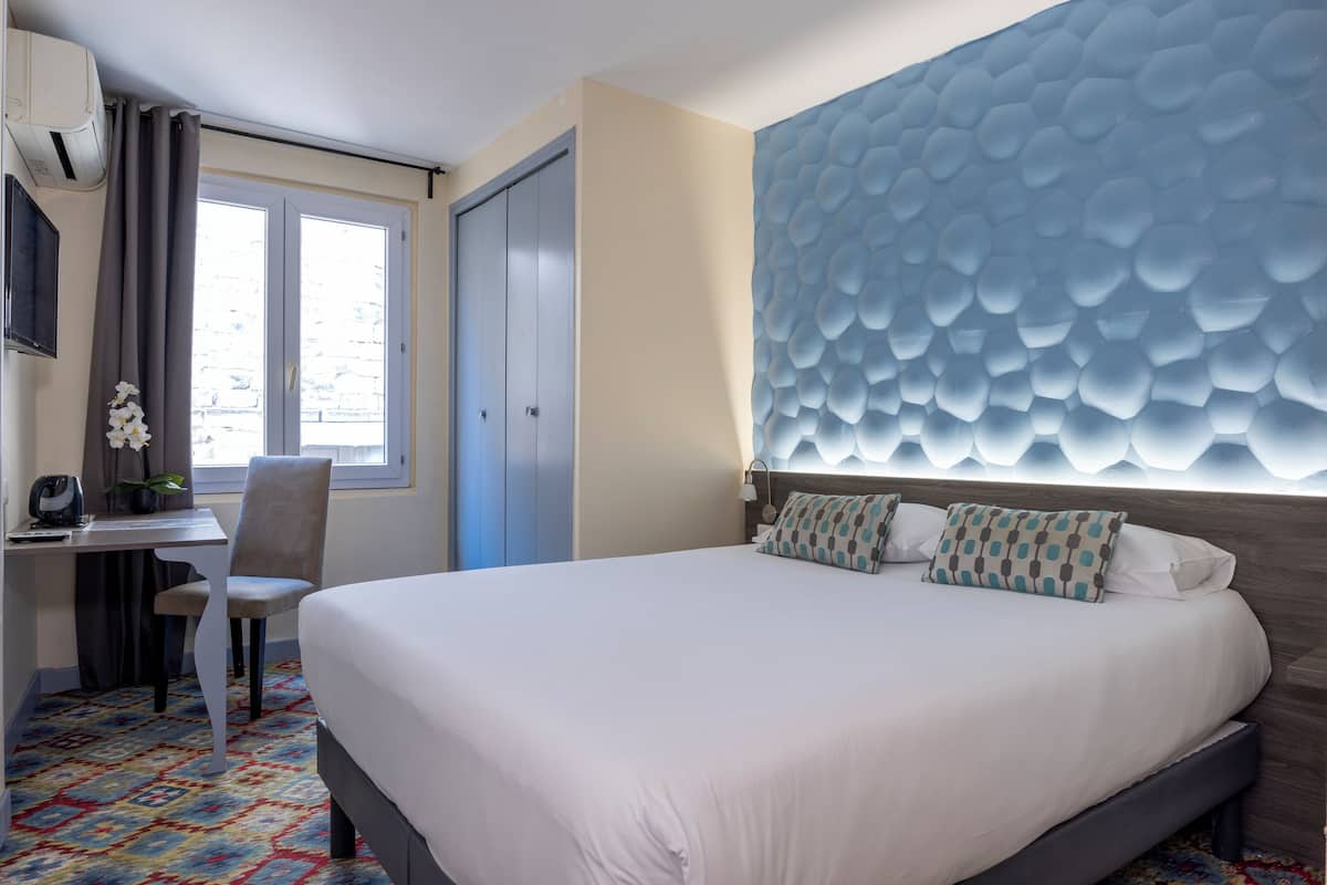 A hotel room with a bed, a desk, a chair, a window, and a decorative wall.