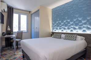 A hotel room with a bed, a desk, a chair, a window, and a decorative wall panel.