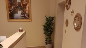 A reception area with a wooden floor, a reception desk, a framed painting of a canal, a potted plant, and decorative mirrors on the wall. - Hôtel Danieli Avignon (Avignon)