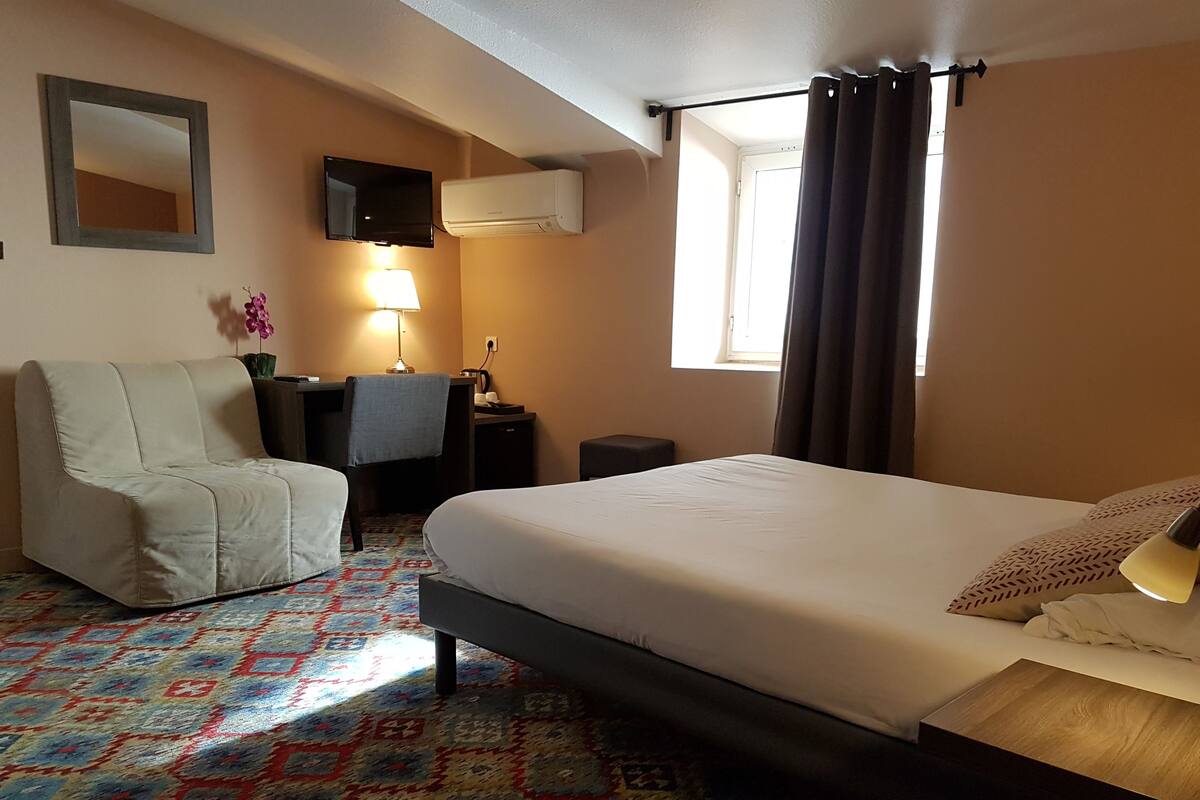 A hotel room with a bed, a desk, a chair, a TV, and a window with curtains.