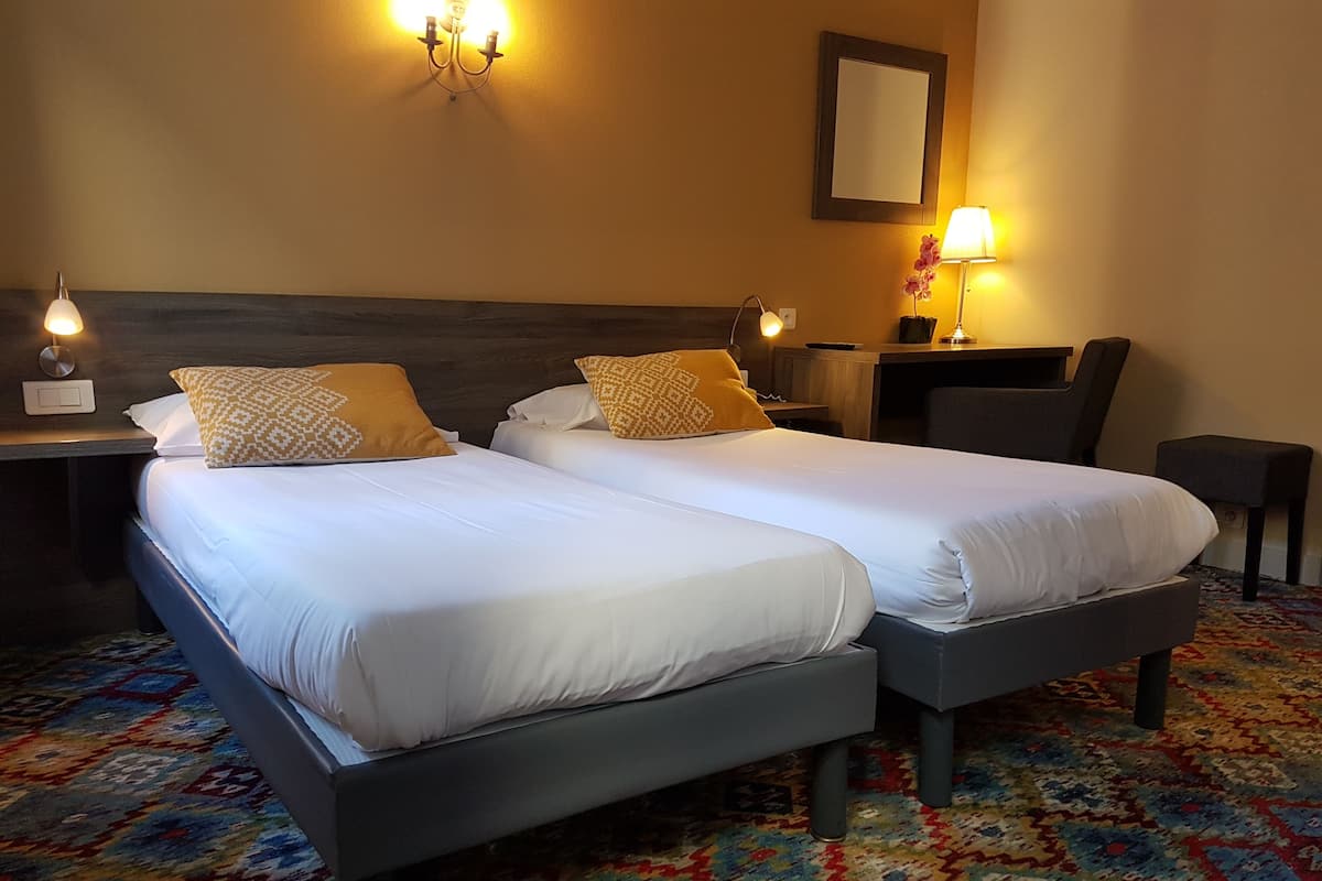 A hotel room with two beds, a desk, a chair, and a patterned carpet.