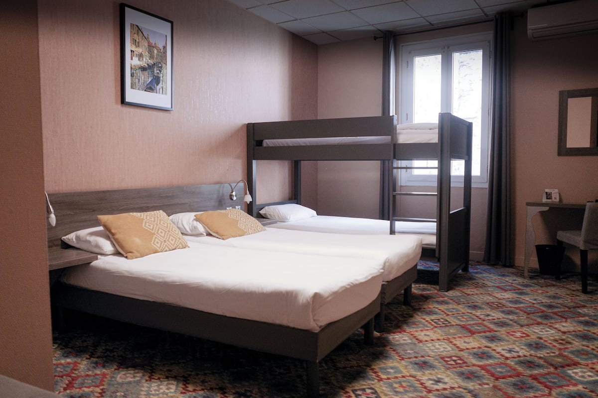 A hotel room with two beds, a bunk bed, a desk, and a patterned carpet.