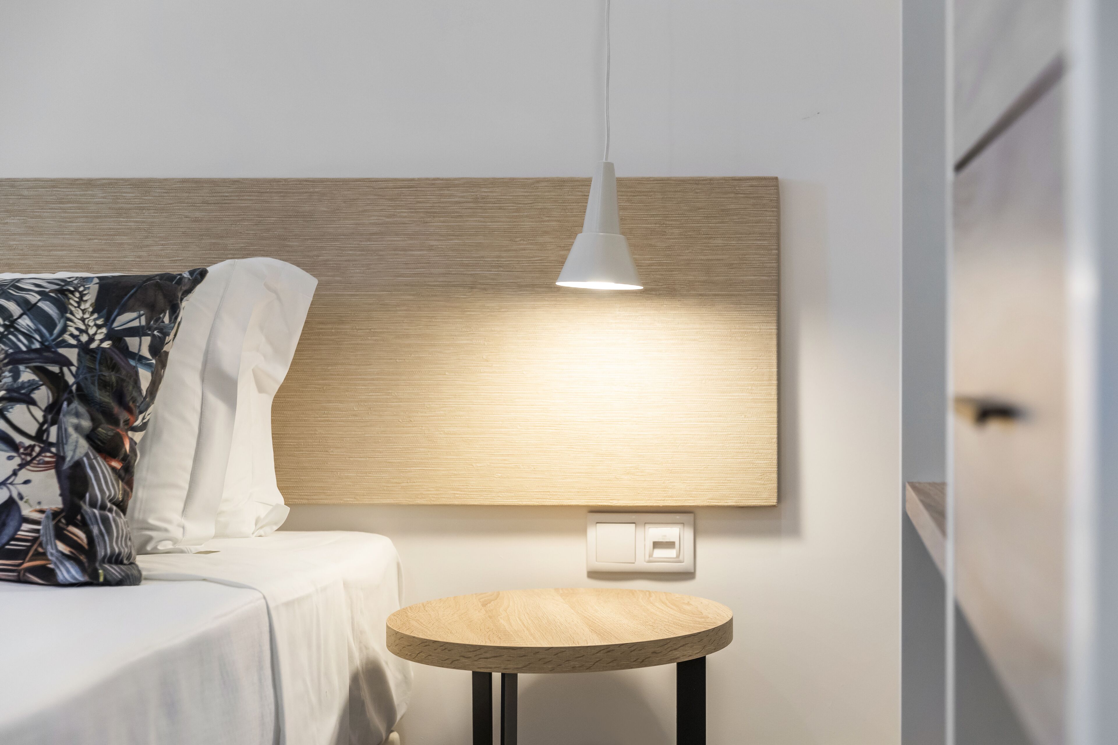 Een moderne hotelkamer met een bed, een rond houten bijzettafeltje en een wandlamp.