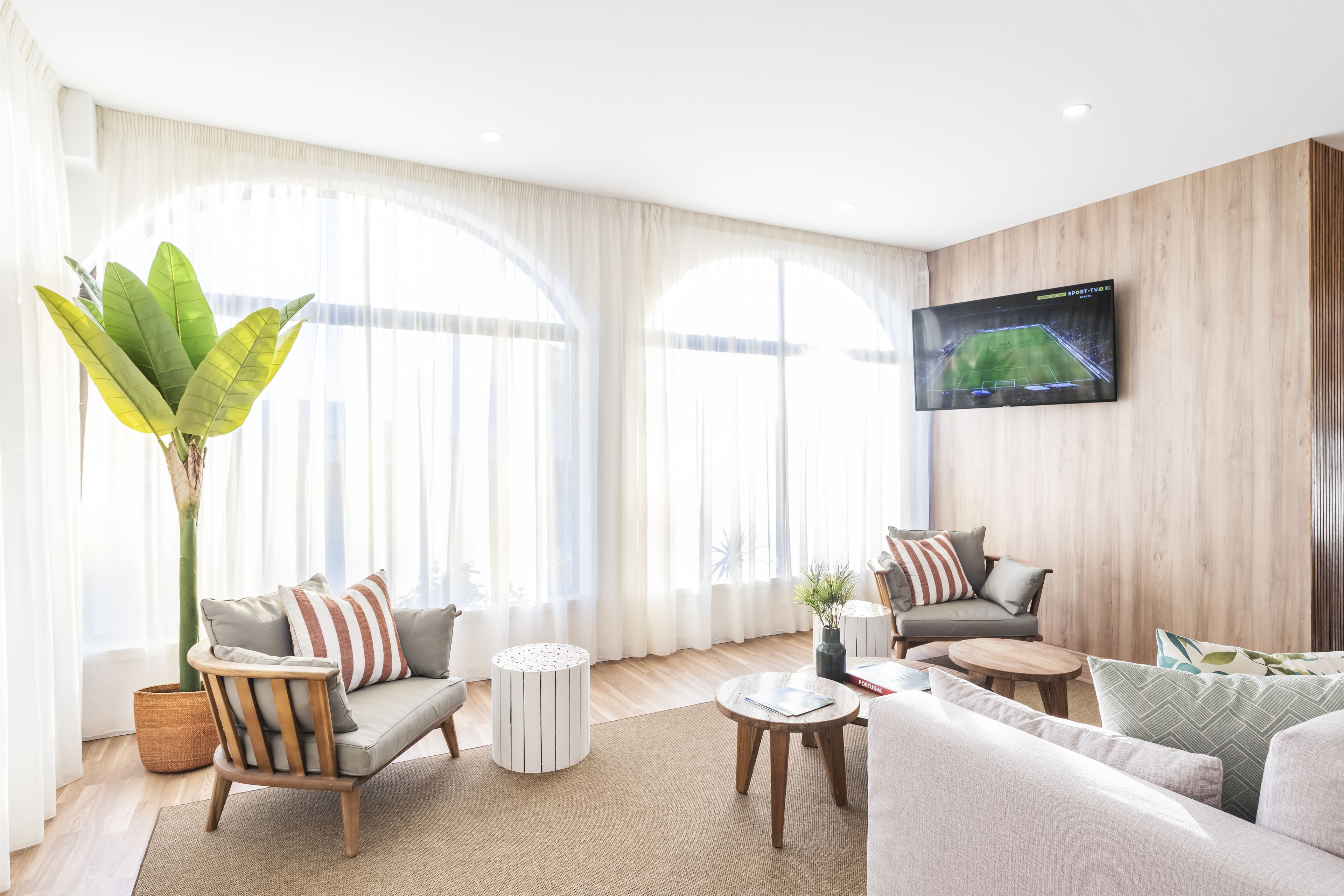 Een moderne woonkamer met een bank, fauteuils, een salontafel en een aan de muur bevestigde televisie.