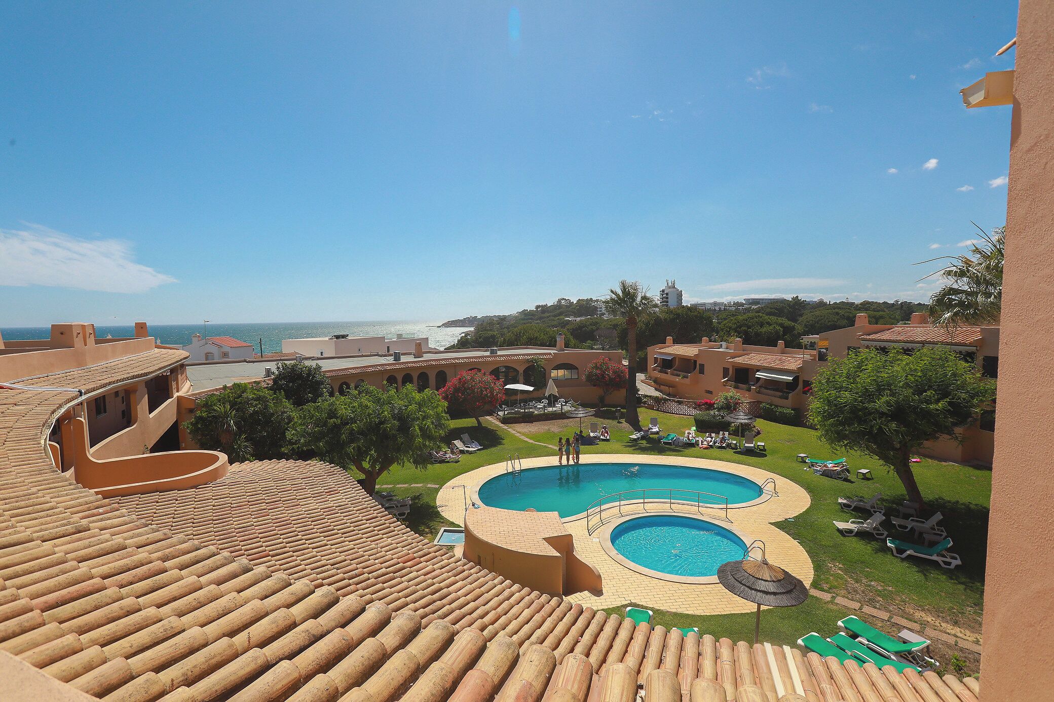 A rooftop pool with a view of the sea, surrounded by lounge chairs and greenery.