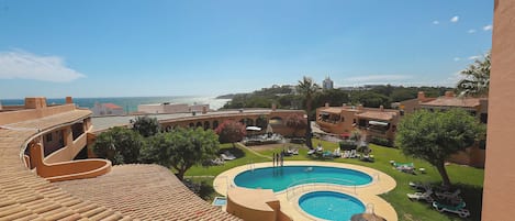 A rooftop pool with a view of the sea, surrounded by lounge chairs and greenery.