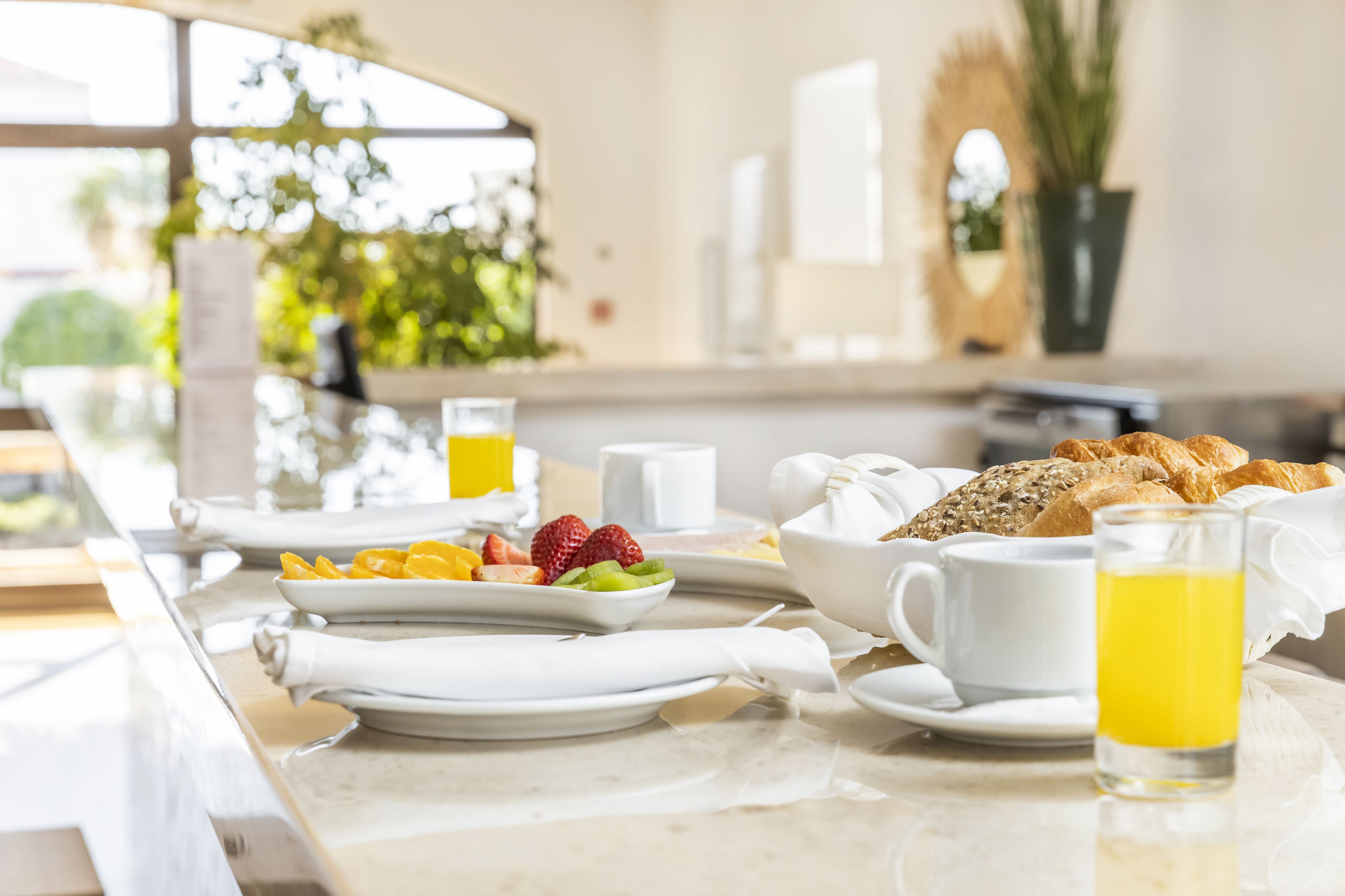 A breakfast setting with plates of fruit, croissants, and a glass of orange juice on a marble countertop.