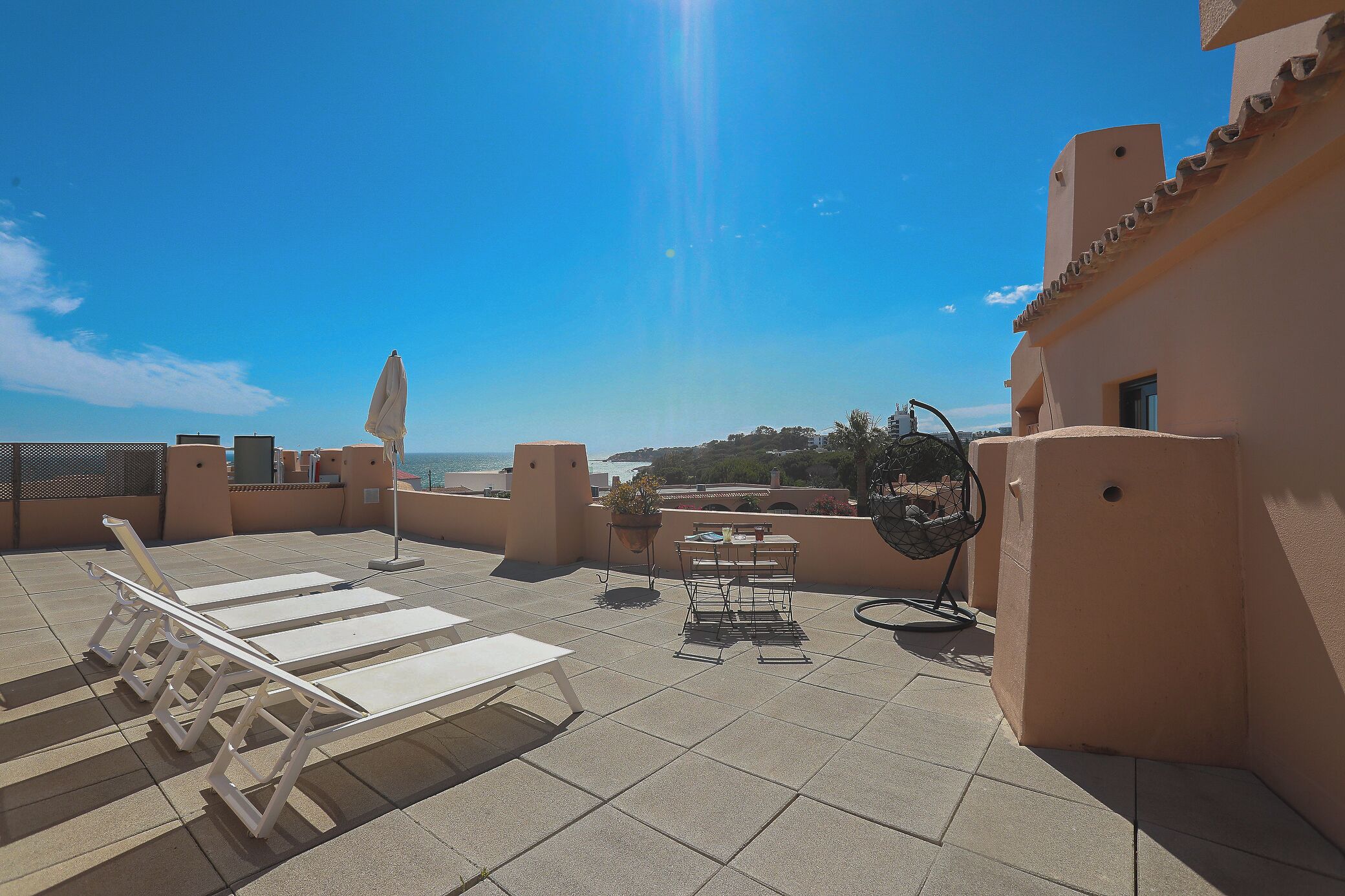 A rooftop terrace with sun loungers, a table, and a chair.