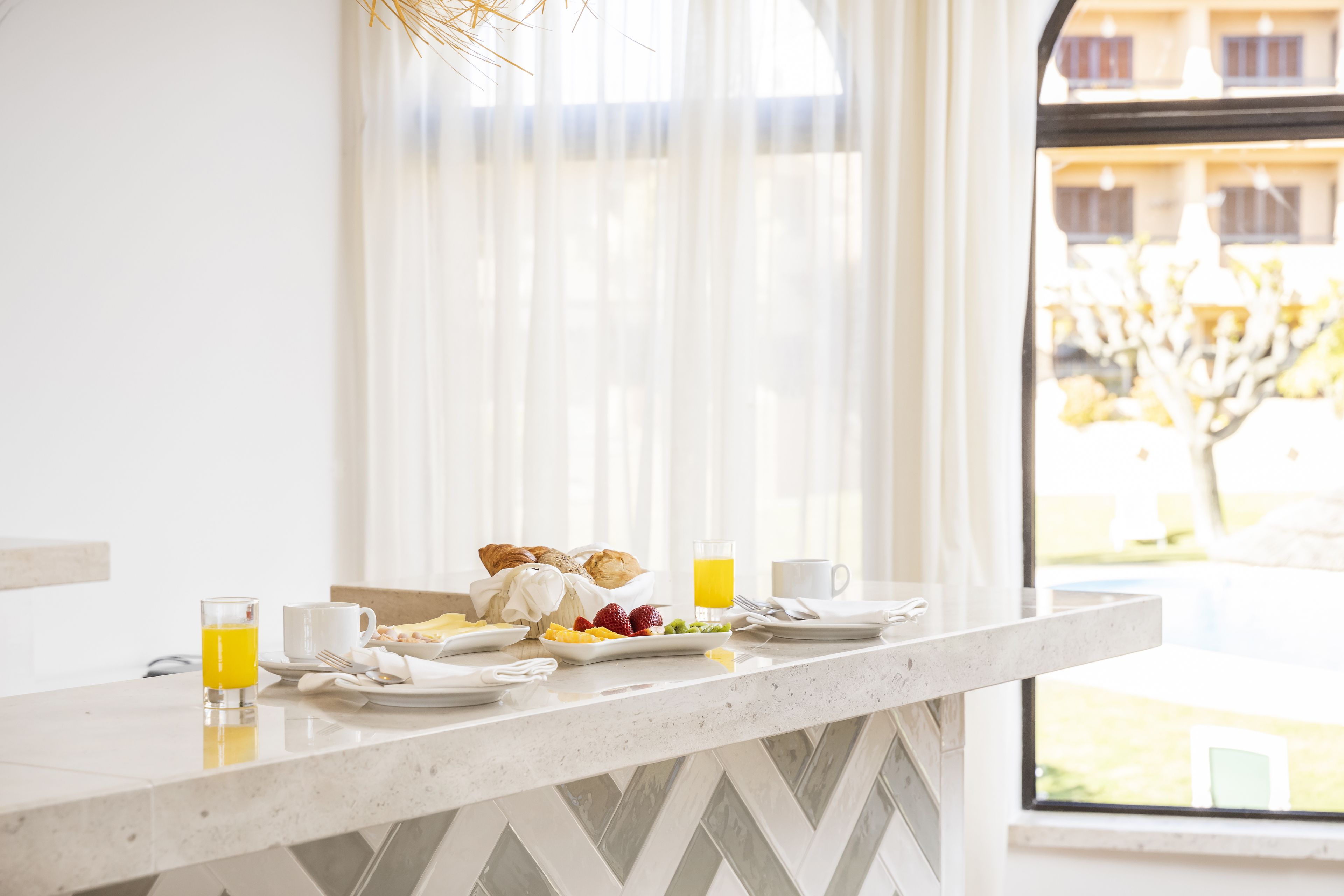 A breakfast setup with croissants, fruit, and orange juice on a marble countertop.