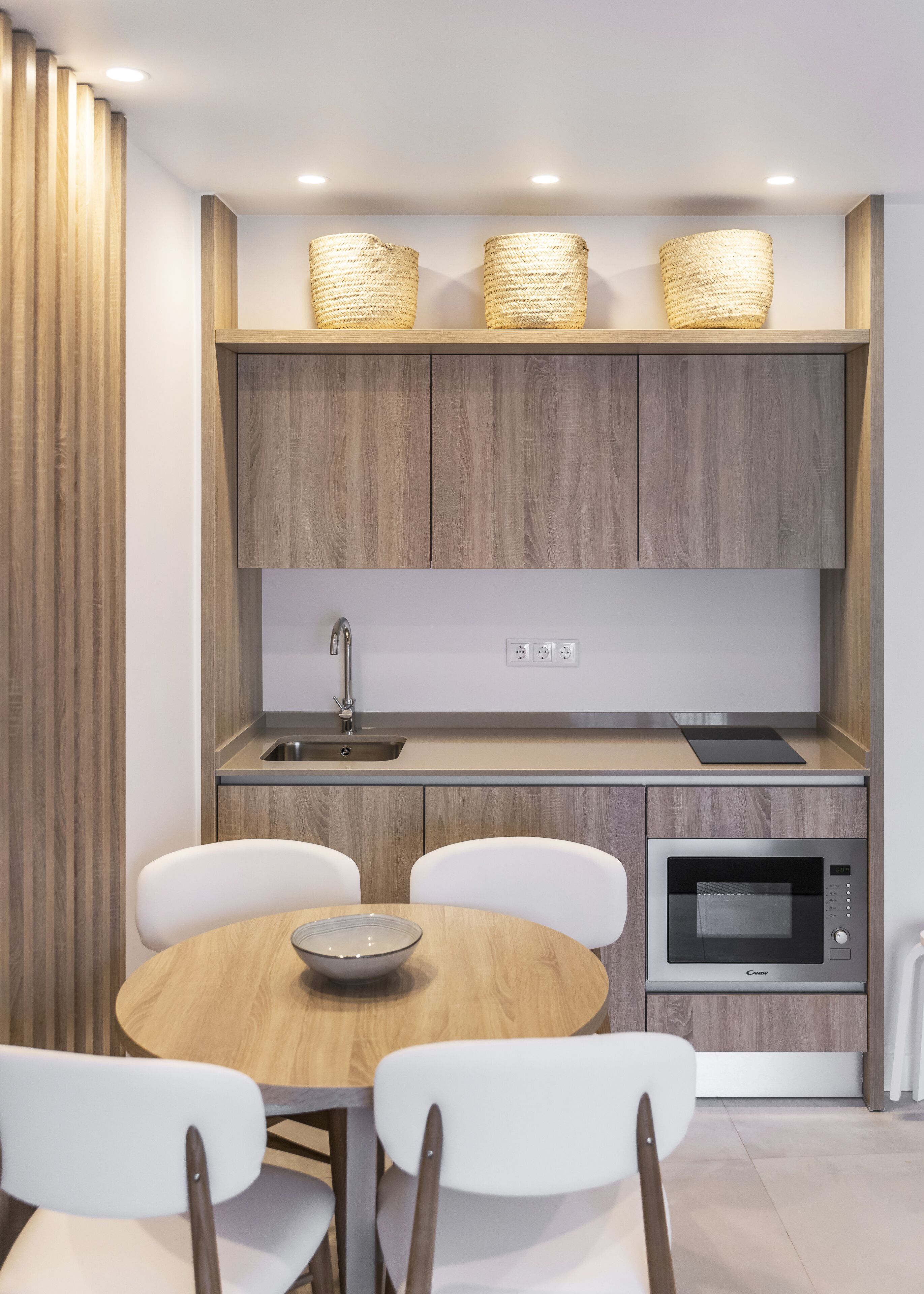 A modern kitchen with wooden cabinets, a sink, a microwave, and a dining table with chairs.