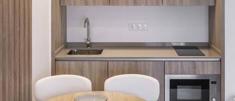 A modern kitchen with wooden cabinets, a sink, a microwave, and a dining table with chairs.