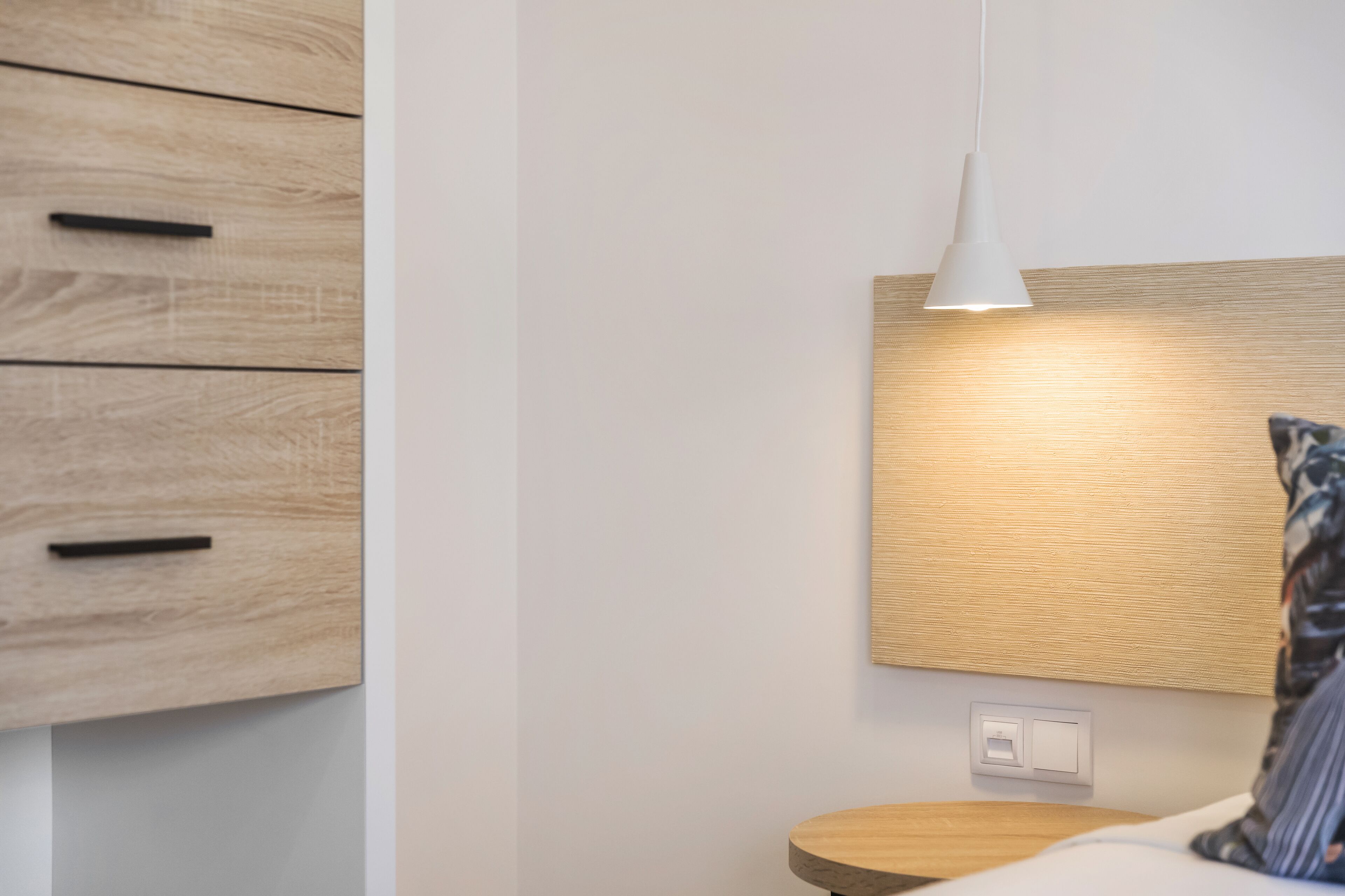 Un dormitorio moderno con cabecera de madera, una mesita de noche y una lámpara colgante.