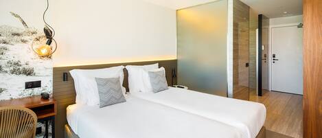 Une chambre d’hôtel avec un grand lit, un bureau avec une chaise, une lampe fixée au mur et une porte donnant sur une autre pièce.