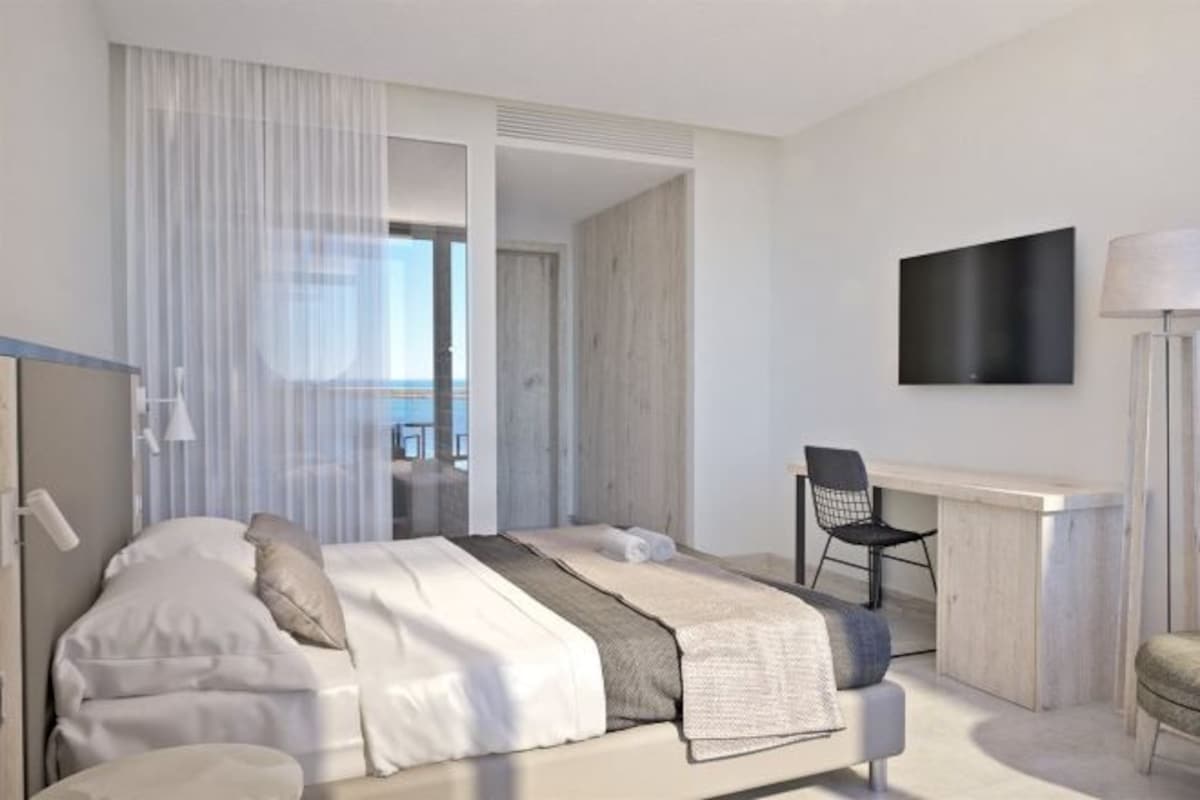 A modern hotel room with a bed, a desk, a chair, and a TV on the wall.