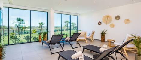 A modern indoor lounge with large windows, black lounge chairs, and a view of a green landscape.