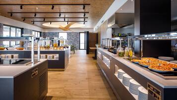 Una mesa de buffet moderna con diversos alimentos, una zona central de servicio y un área de descanso con mesas y sillas.