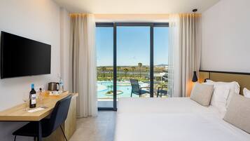 A hotel room with a bed, a desk with a bottle of wine, a chair, a TV, and a view of a pool and landscape.
