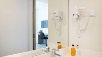 A modern bathroom with a large mirror, a white sink, two hair dryers mounted on the wall, and two bottles of toiletries on the counter.