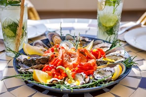 Una bandeja de mariscos con camarones, mejillones y rebanadas de limón sobre un plato azul, acompañada de dos vasos de bebidas heladas con menta y lima.