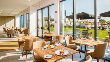 A modern dining area with tables and chairs, large windows, and a view of the outdoor patio.