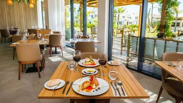 Un ristorante con tavoli e sedie in legno, ampie finestre e vista sul verde.