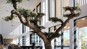 A modern indoor space with a large bonsai tree centerpiece, a checkered floor pattern, and a seating area with tables and chairs. - AP Cabanas Beach & Nature - Adults Friendly (Tavira)