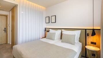 A hotel room with a large bed, a bedside table, a wall-mounted lamp, and a door.