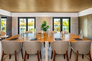 Un salón de conferencias con una mesa de madera, sillas color beige y puertas de vidrio que dan a una zona de piscina.