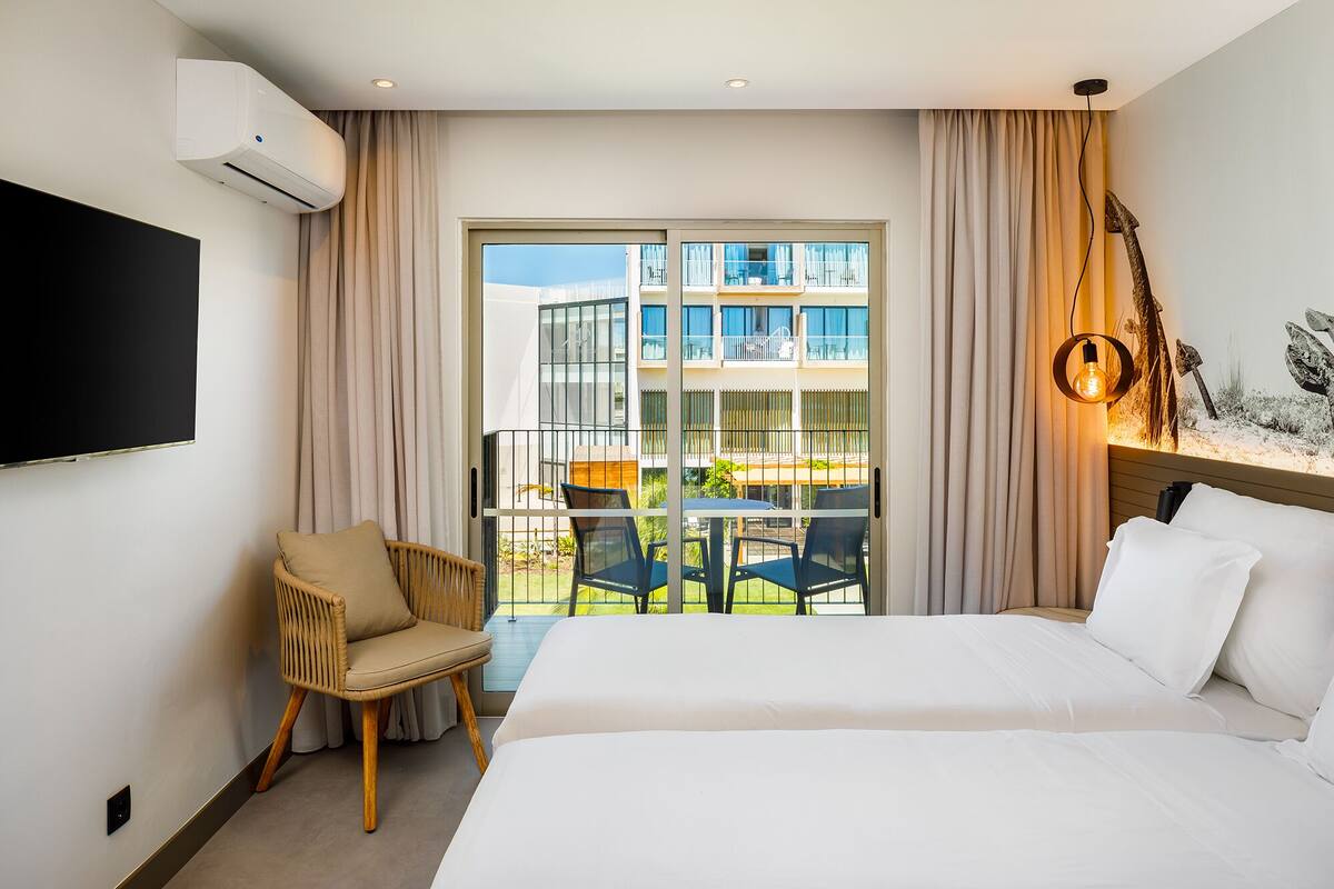 Et hotelværelse med seng, fjernsyn, stol, balkon med bord og stole samt en dekorativ lampe.