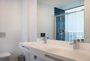 Un baño moderno con un lavamanos blanco, un espejo y una zona de ducha.