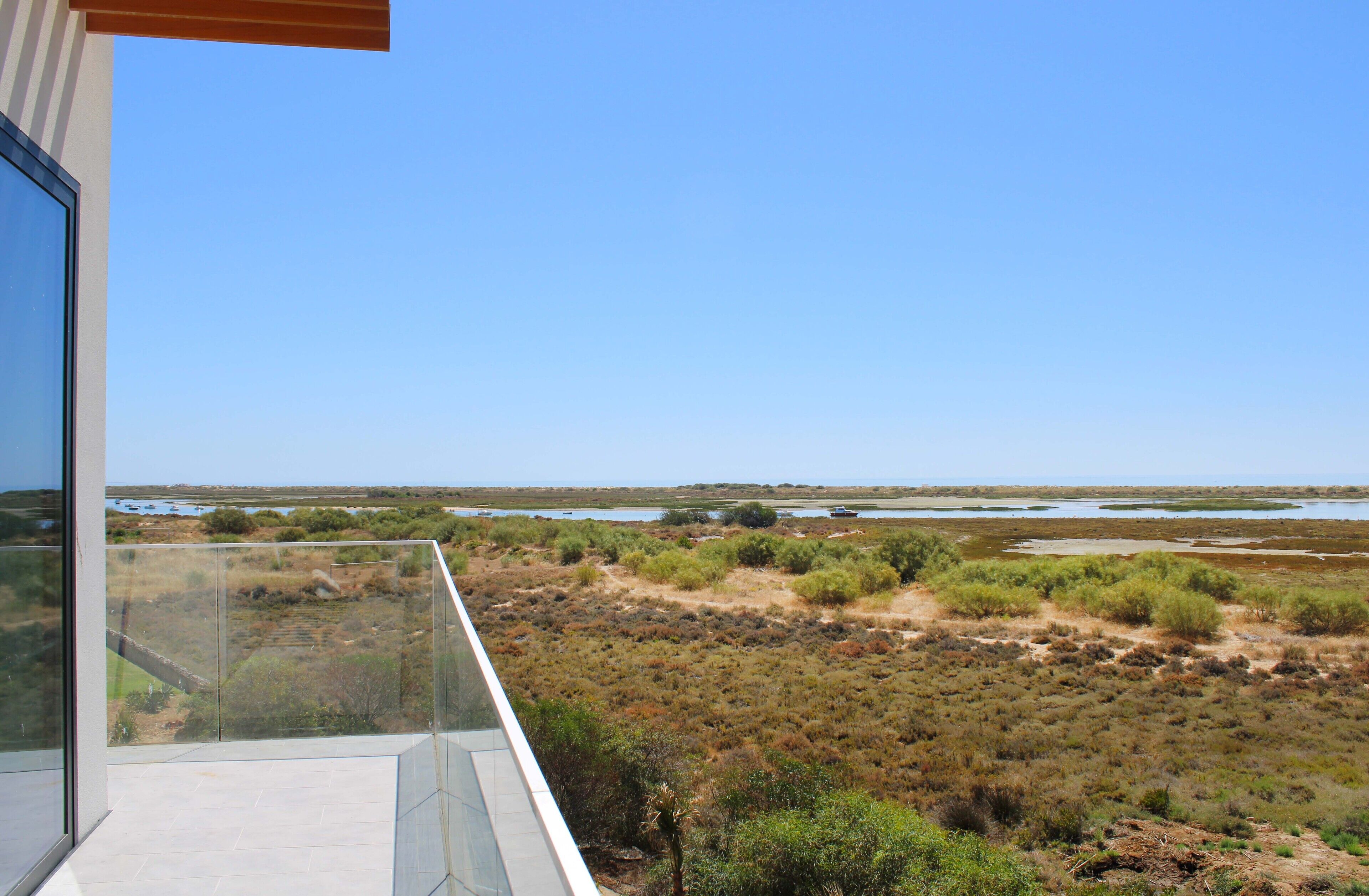 Un balcon offrant une vue sur un paysage côtier, comprenant une plage et une étendue d’eau.
