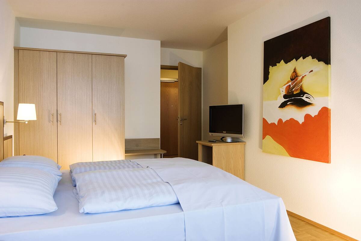 Ein Hotelzimmer mit Bett, Fernseher und einem Gemälde an der Wand.