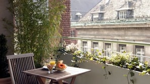 En balkon med et træbord og stole, plantekrukker og udsigt til bygninger.