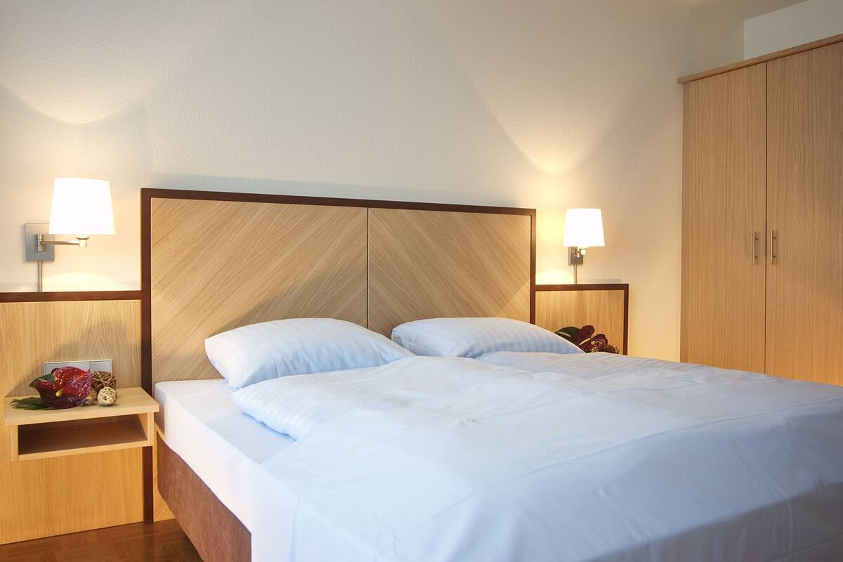 Ein Hotelzimmer mit einem großen Bett, einem hölzernen Kopfteil, zwei Nachttischen mit Lampen und einem Kleiderschrank.