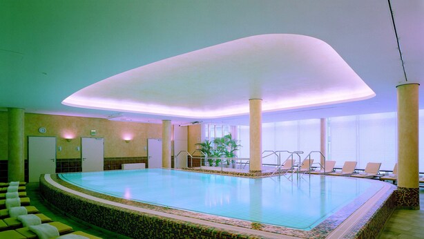 En stor indendørs swimmingpool med flisebelagt kant, liggestole og flisegulv.