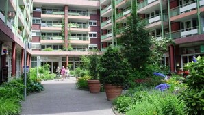 En flereetagers boligbygning med altaner, en central gårdsplads med plantekasser, og en tydelig indgang.