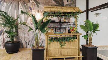 Un petit kiosque en bambou, doté d’une étagère où sont exposées des boissons en bouteille, et entouré de plantes en pot.