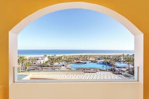 Vista de un resort a través de un ventanal arqueado, con piscina, playa y océano.