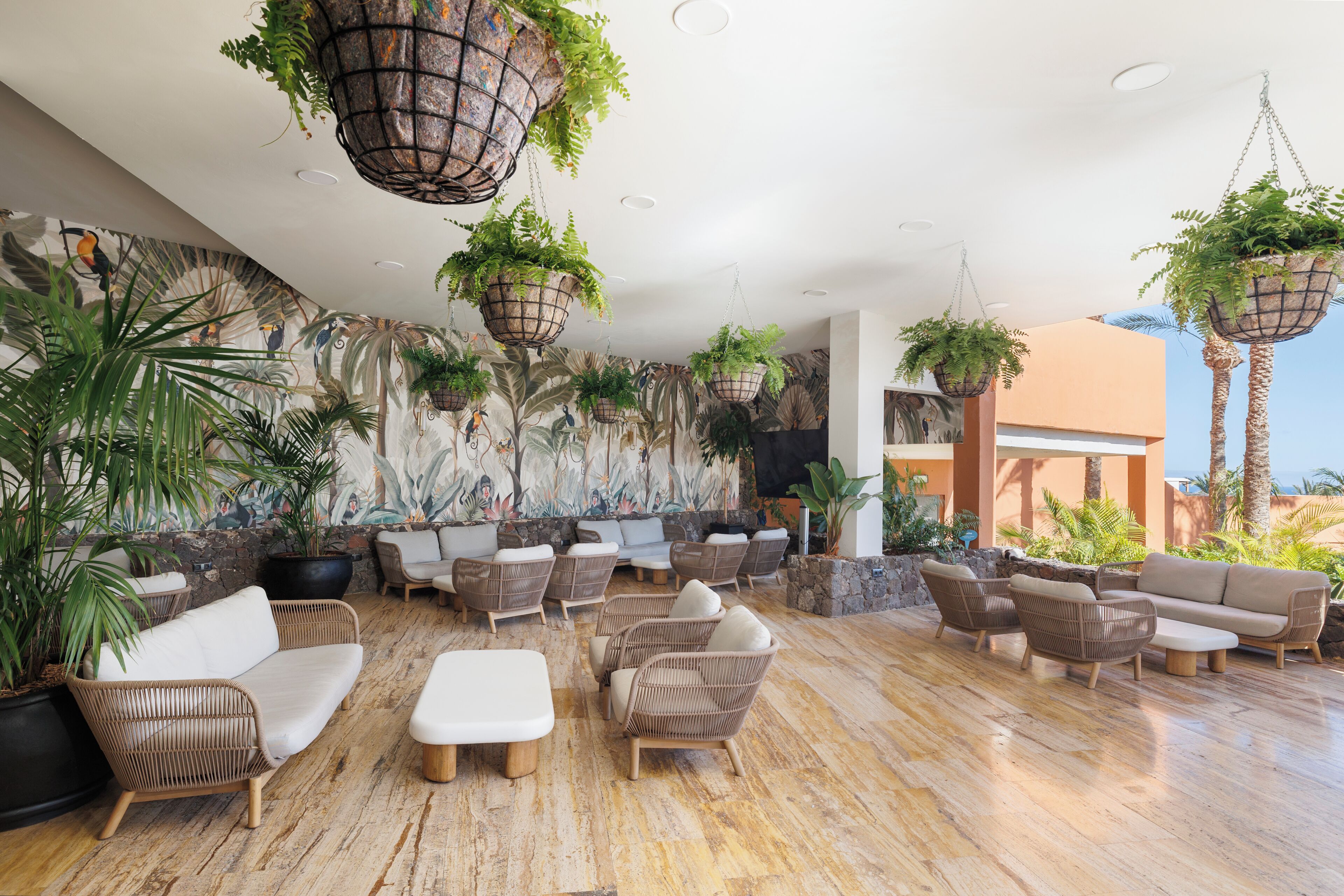 Un área de descanso con muebles de mimbre, plantas colgantes y un mural.