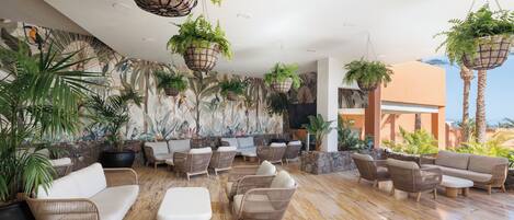 Un área de descanso con muebles de mimbre, plantas colgantes y un mural.