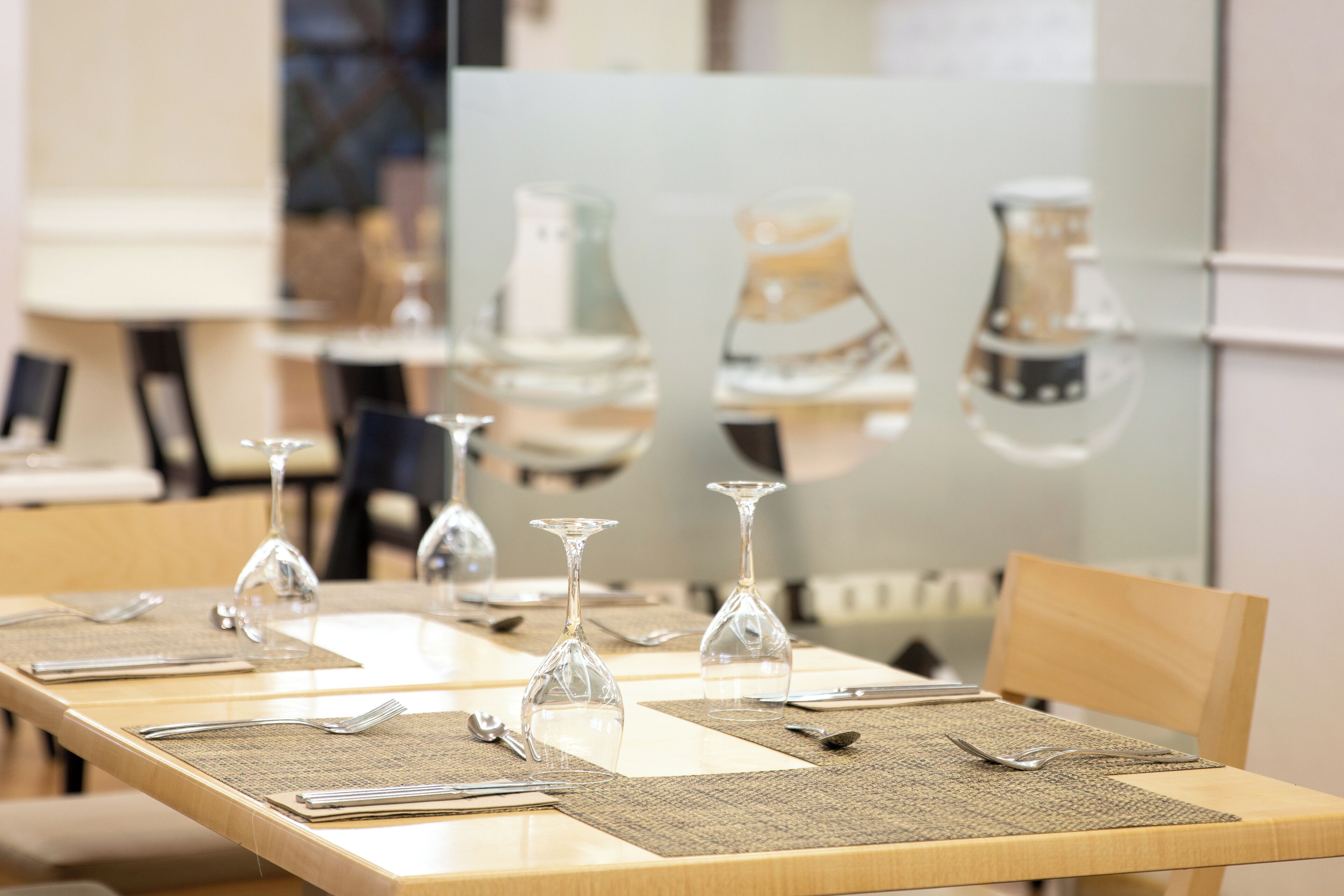 Una mesa de comedor dispuesta con cristalería, cubiertos y manteles individuales.