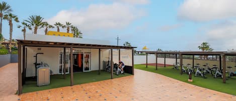 An outdoor gym area with exercise bikes, a covered seating area, and a luggage trolley.