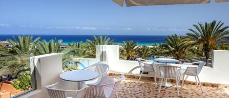 A terrace with a view of the ocean, white chairs, a round table, and a large umbrella.