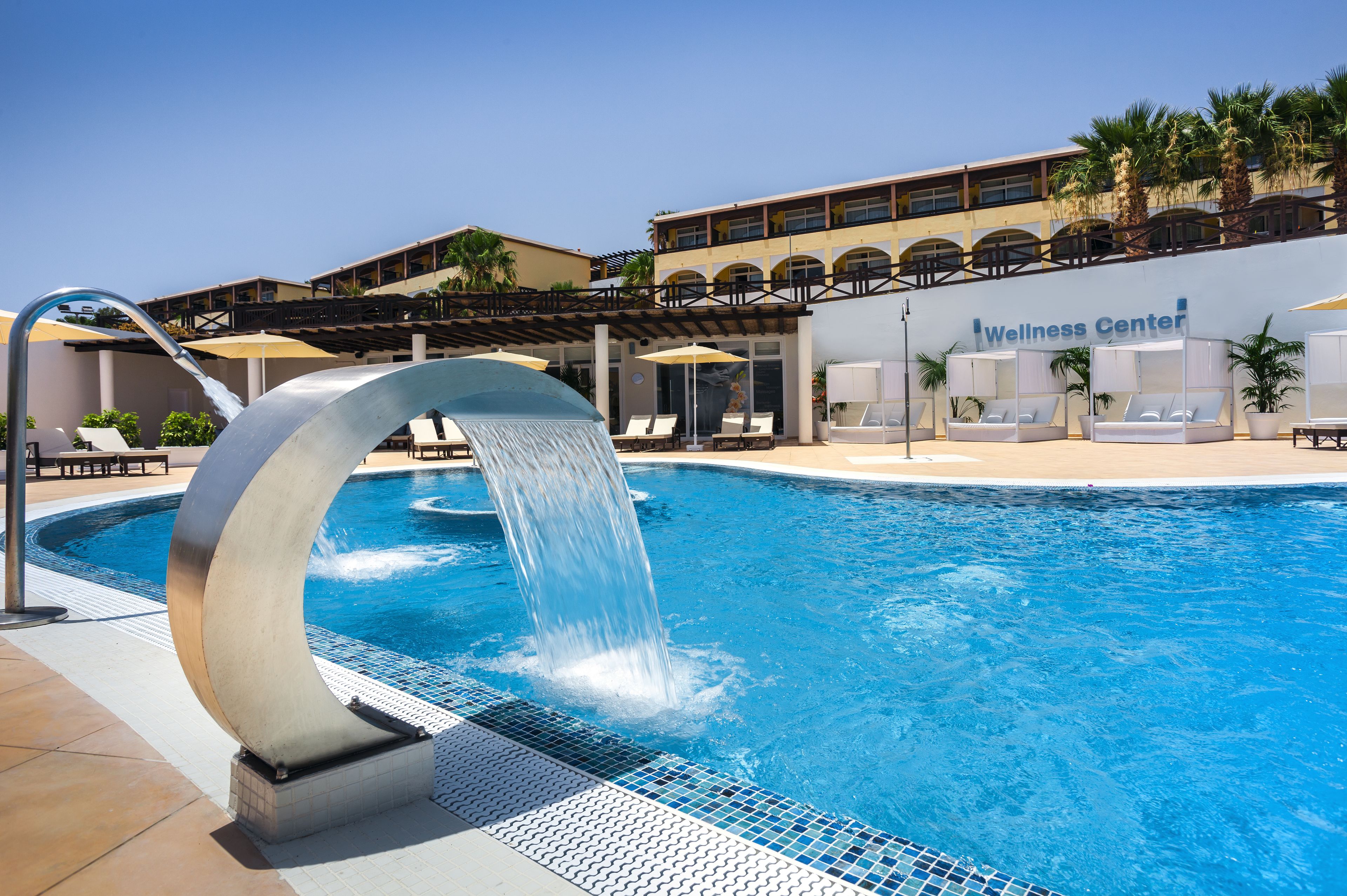 A swimming pool with a water feature, lounge chairs, and a Wellness Center in the background.